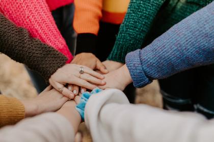 a group of people with lots of colourful knit jumpers on have put their hands all together in the spirit of teamwork.