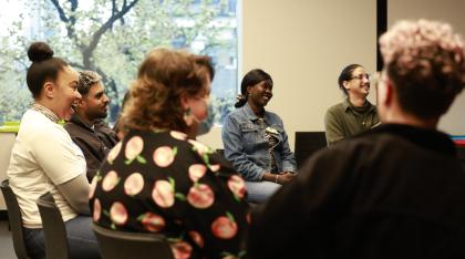A group of young adults sitting on chairs in a circle smiling and laughing.