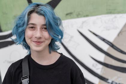 Young person with blue hair and a black T-shirt smiling