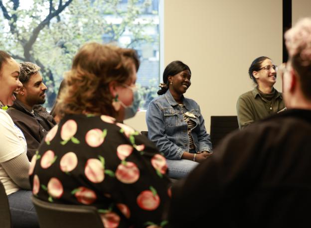 A group of young adults sitting on chairs in a circle smiling and laughing.