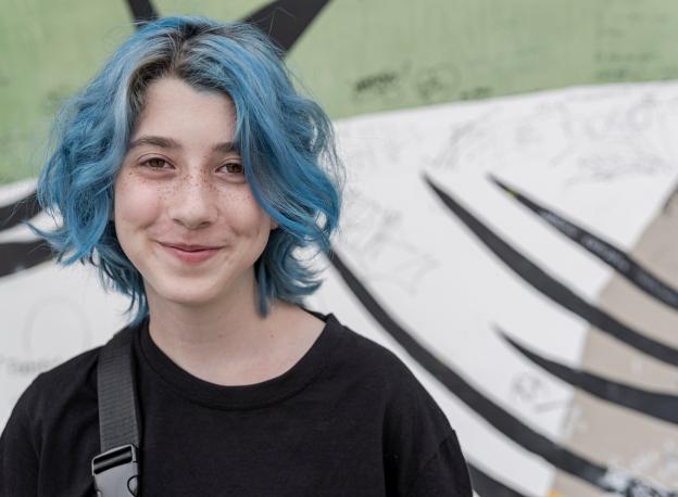 Young person with blue hair and a black T-shirt smiling